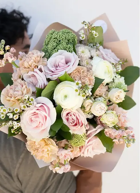 Bouquet of delicate pink and white roses, green chrysanthemums and small flowers, wrapped in white paper,