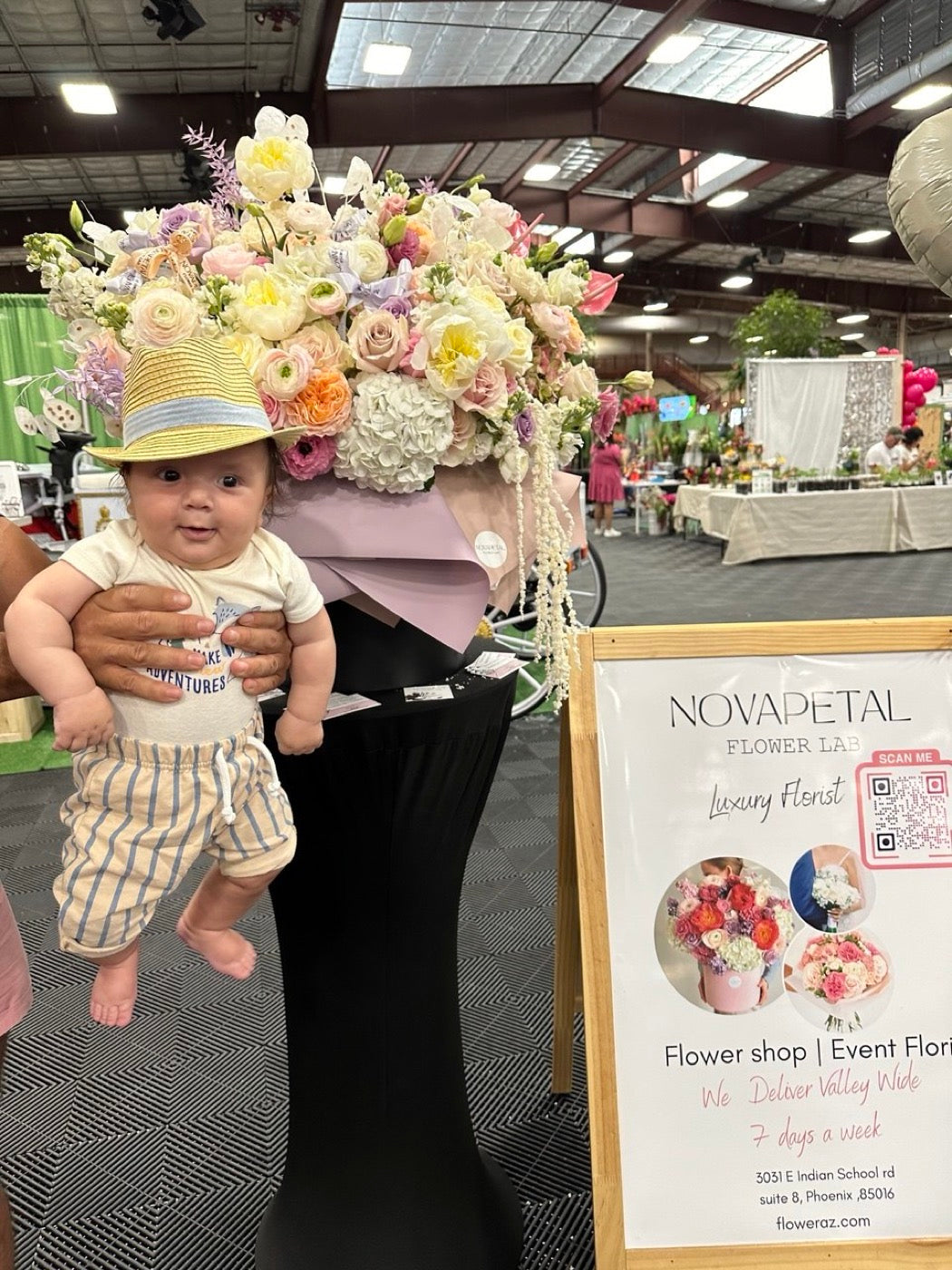 The founders son at a Novapetal stand at the Novapetal stand at a Phoenix flower show, beside a tall pastel arrangement and the Novapetal Flower Lab sign