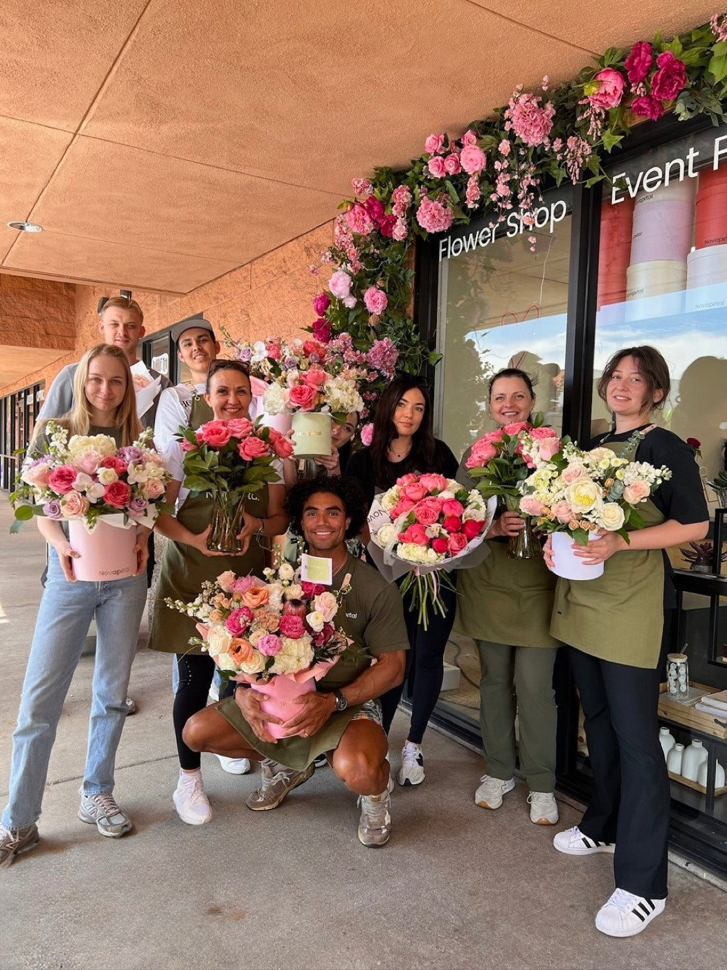 The Novapetal team outside the Arcadia studio in Phoenix, holding hand-tied bouquets and hat boxes under a floral installation over the shop entrance