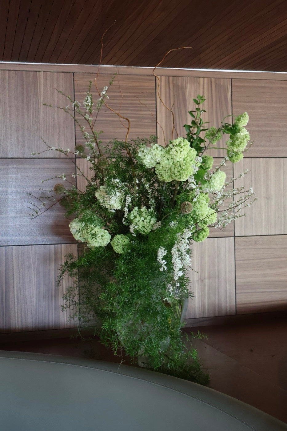 Green and white viburnum and spirea arrangement by Novapetal Flower Lab on a banquette table, set against wood panelling in a Phoenix restaurant