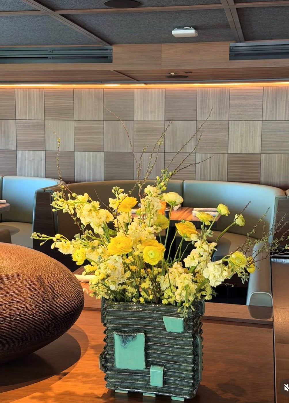 Yellow arrangement by Novapetal Flower Lab with ranunculus, snapdragon and orchid in a ceramic vessel, on a table in a Phoenix restaurant lounge