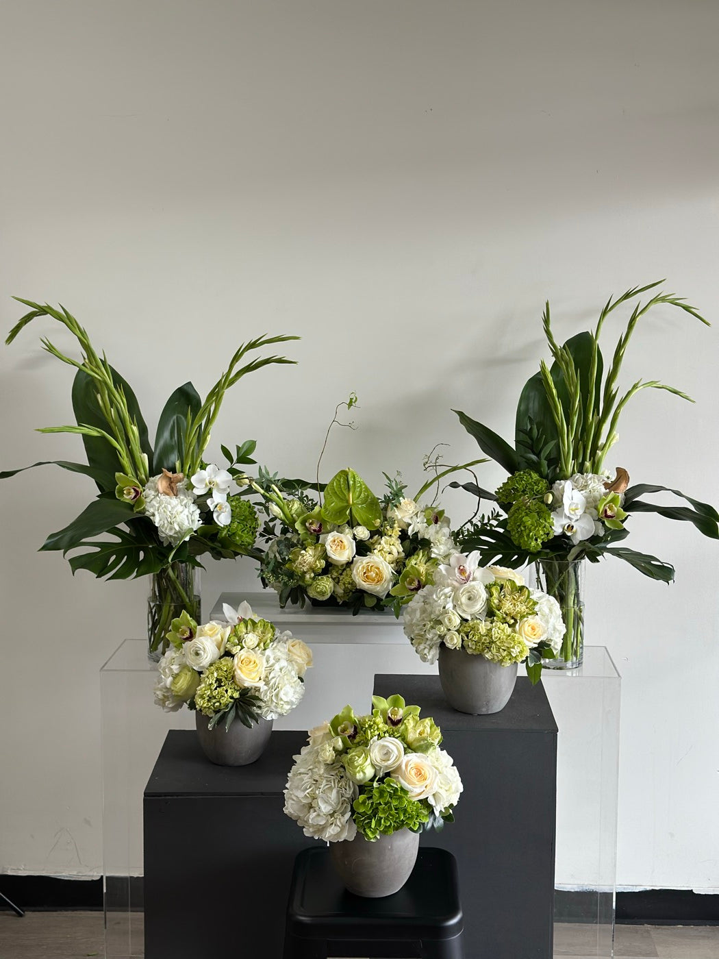 A set of six white and green arrangements by Novapetal Flower Lab staged in the Phoenix studio before delivery, with hydrangea, garden roses, gladioli and tropical leaves