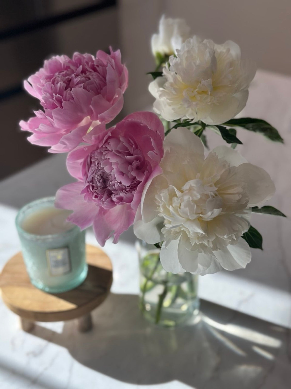 Pink and white peonies in a small glass vase on a kitchen counter