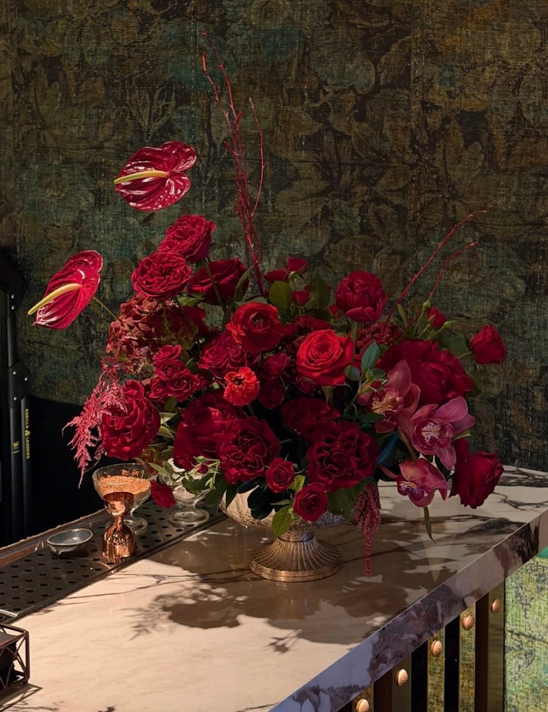 Close-up of the red bar arrangement by Novapetal Flower Lab, with anthurium and hanging amaranthus against the dark wall