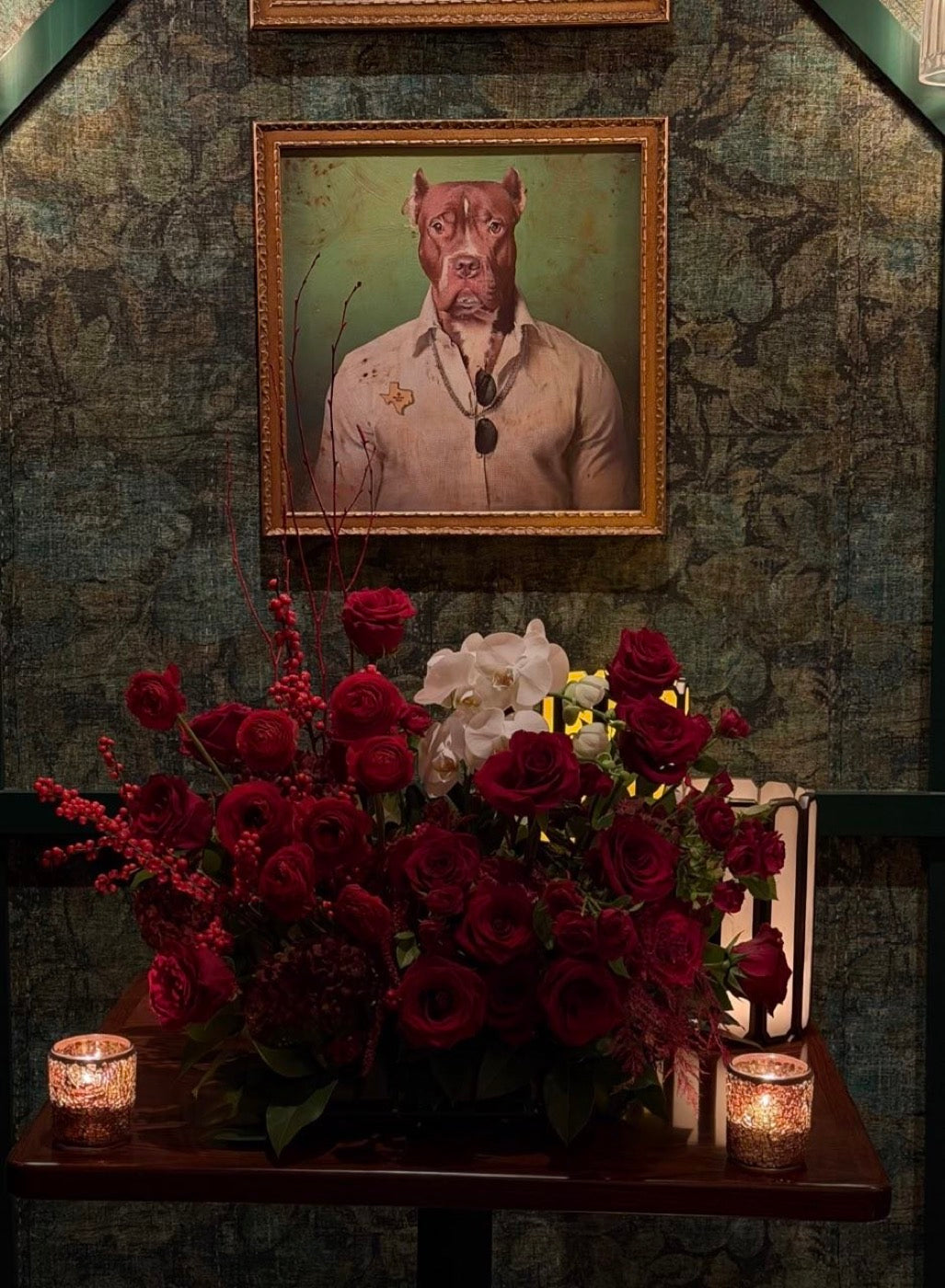 Red roses and white phalaenopsis orchids by Novapetal Flower Lab on a side table at the same event, lit by candles beneath a framed portrait