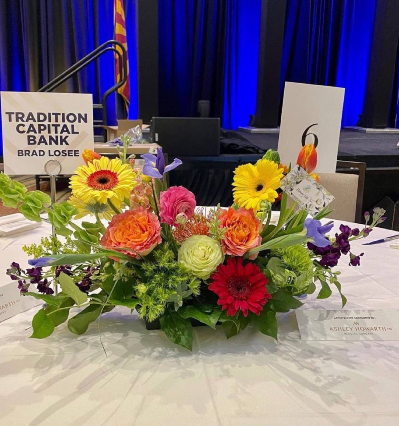 Bright gala centerpiece by Novapetal Flower Lab with yellow gerbera, orange garden roses, pink ranunculus, iris and pincushion protea on a sponsor table