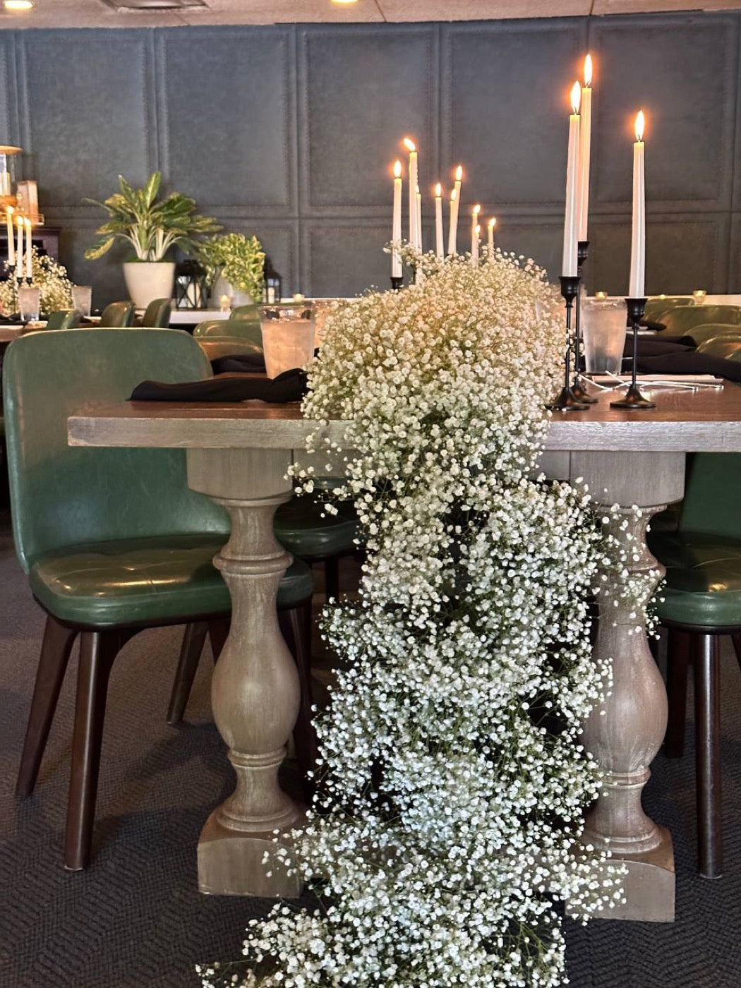 Cascading gypsophila table runner by Novapetal Flower Lab spilling from a restaurant table set with black taper candles