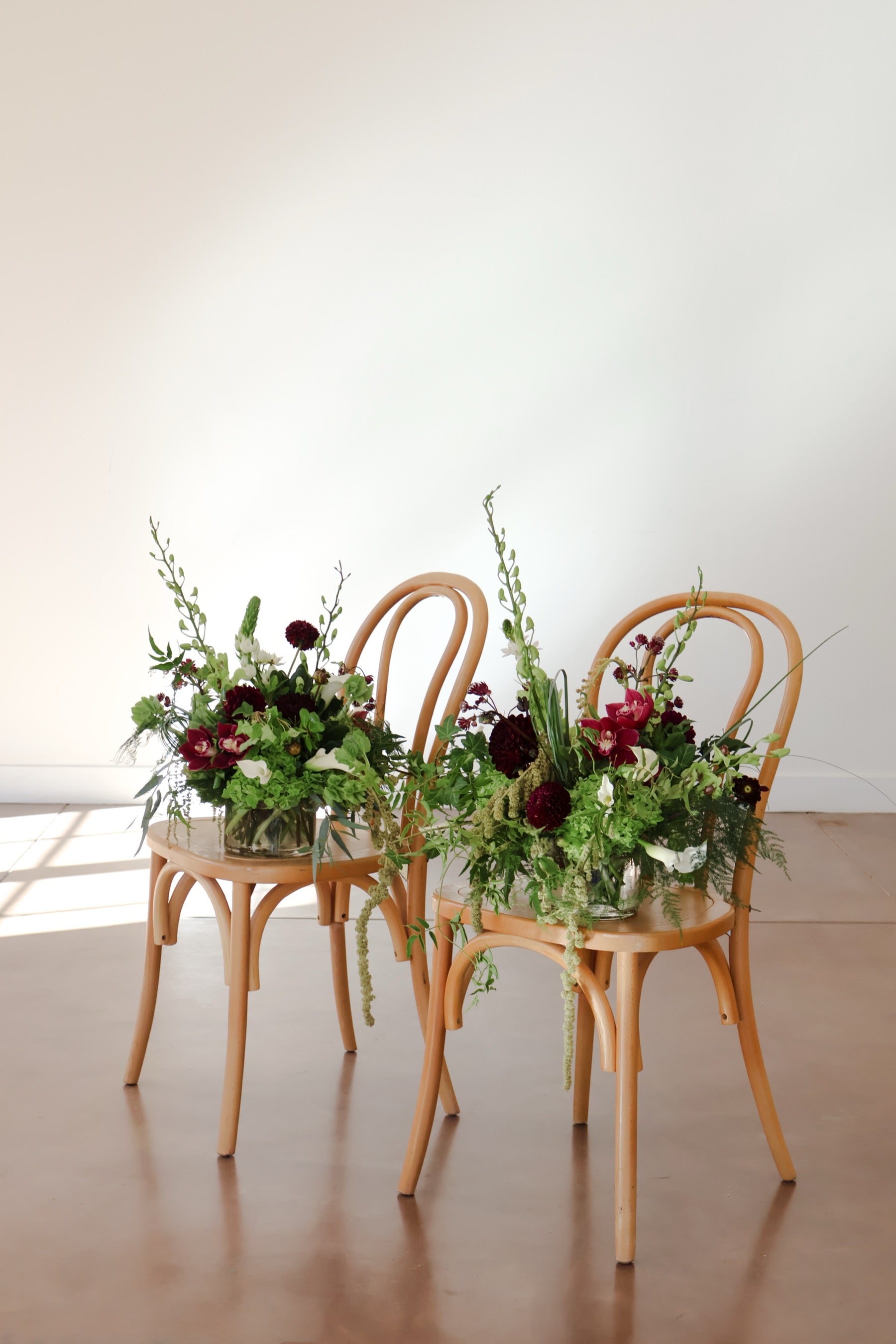 Pair of burgundy and green arrangements by Novapetal Flower Lab on bentwood chairs, with green hydrangea, calla lilies and cymbidium orchids