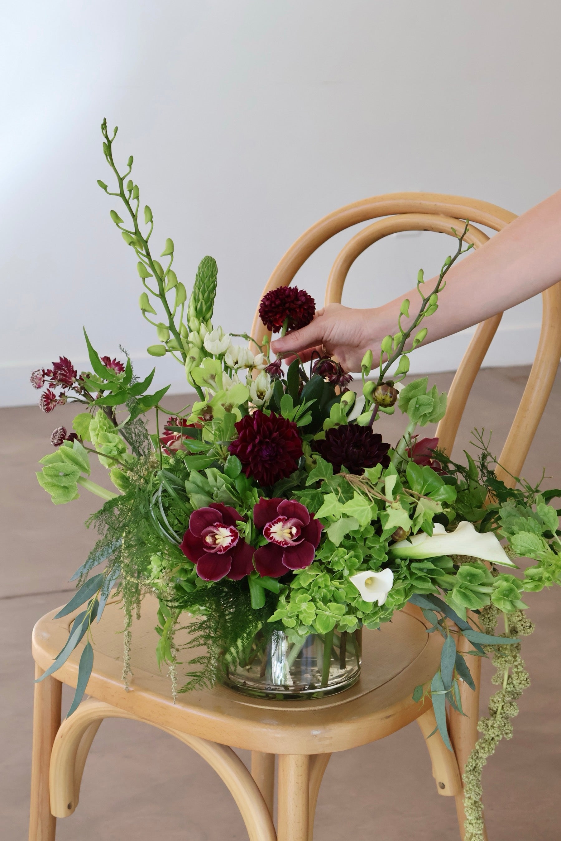 Novapetal Flower Lab florist placing a burgundy dahlia into a green hydrangea and ivy arrangement with white calla lilies
