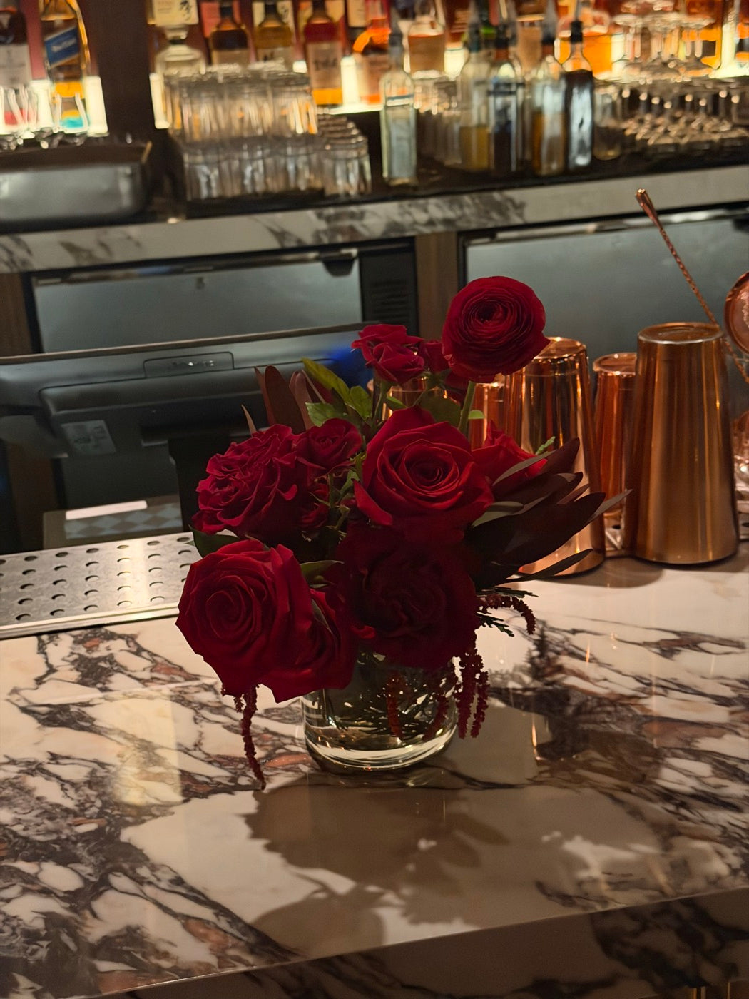 Small red rose and ranunculus arrangement by Novapetal Flower Lab on the service bar, beside copper cocktail tins
