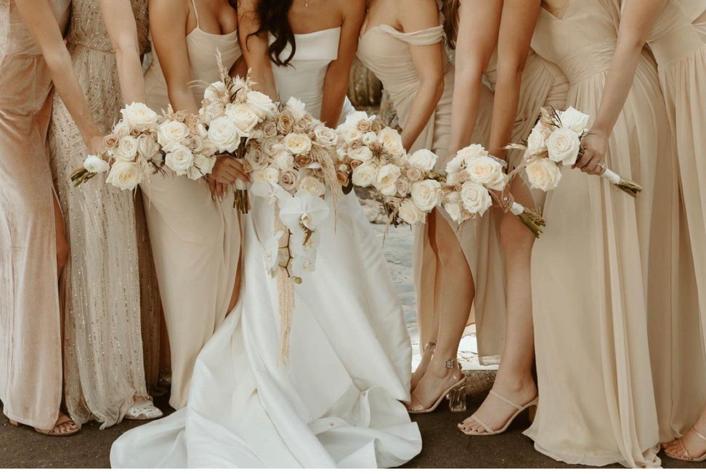 Bride and five bridesmaids in champagne dresses holding hand-tied bouquets of white and blush roses, ranunculus and dried grasses by Novapetal Flower Lab at a Phoenix wedding