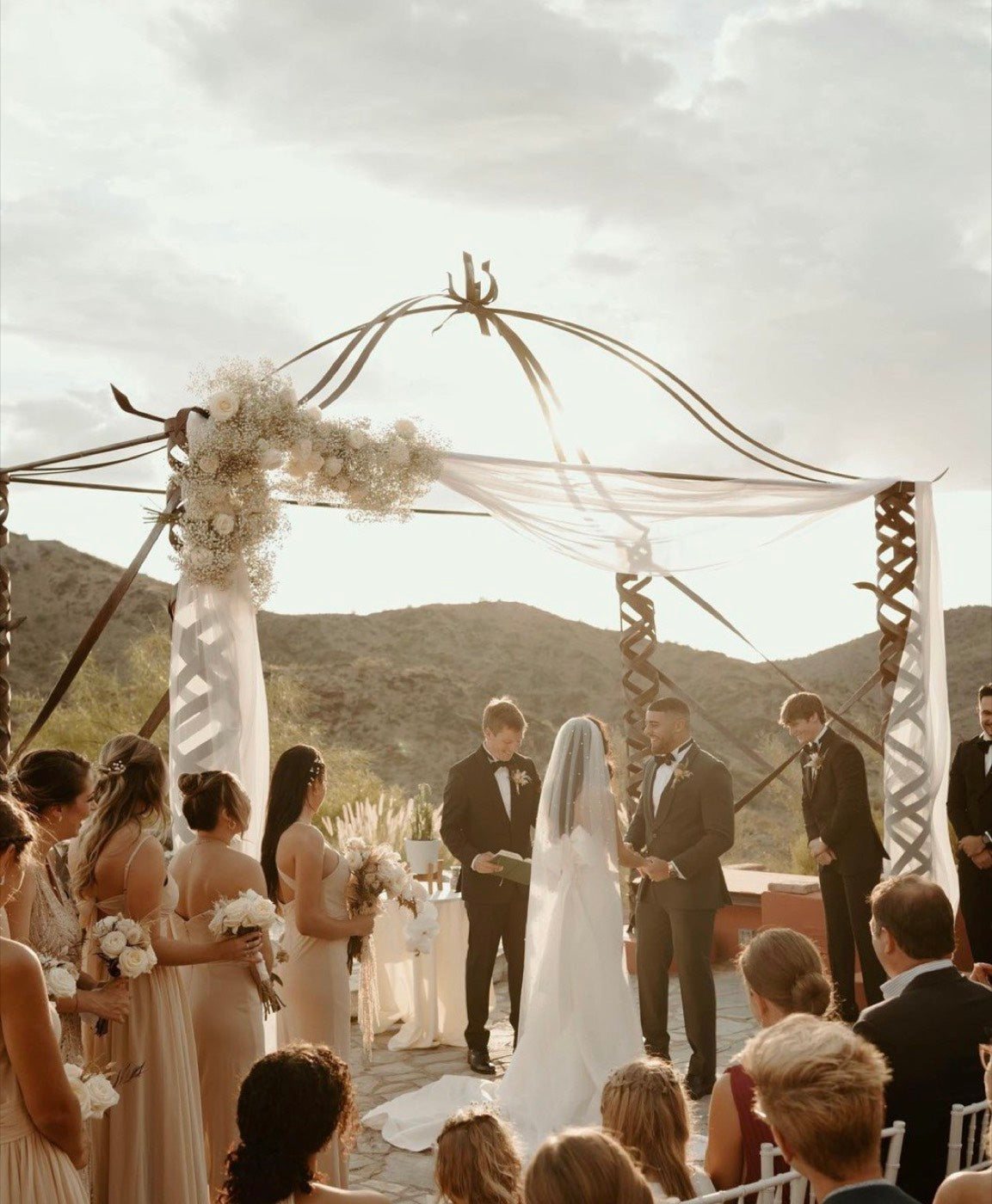 Boho ceremony arch by Novapetal Flower Lab, wrapped in dried pampas and ribbon against the Phoenix mountains, with the couple at the altar