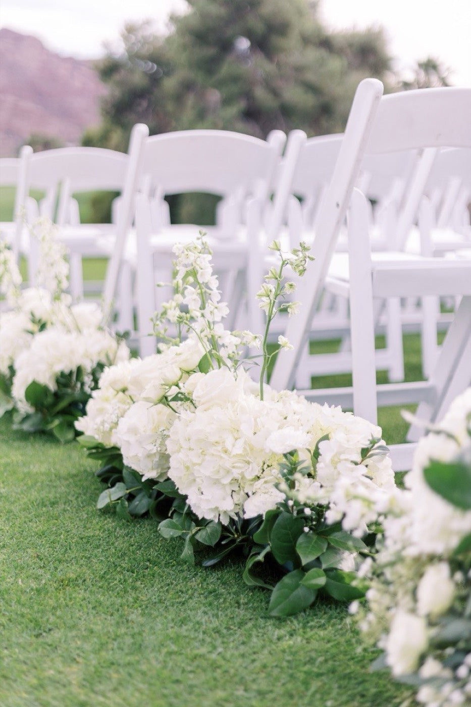 Aisle florals by Novapetal Flower Lab — white hydrangea, stock and eucalyptus laid along rows of white chairs