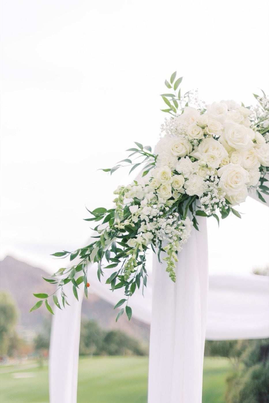 Corner piece of white roses, hydrangea and olive branches by Novapetal Flower Lab on a draped ceremony arch