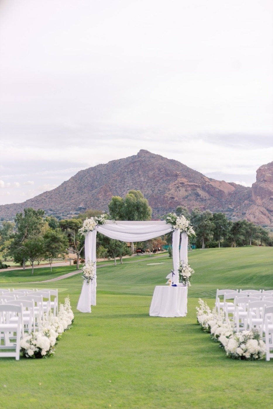The same white ceremony arch by Novapetal Flower Lab seen down the aisle, with the mountains and the lawn beyond