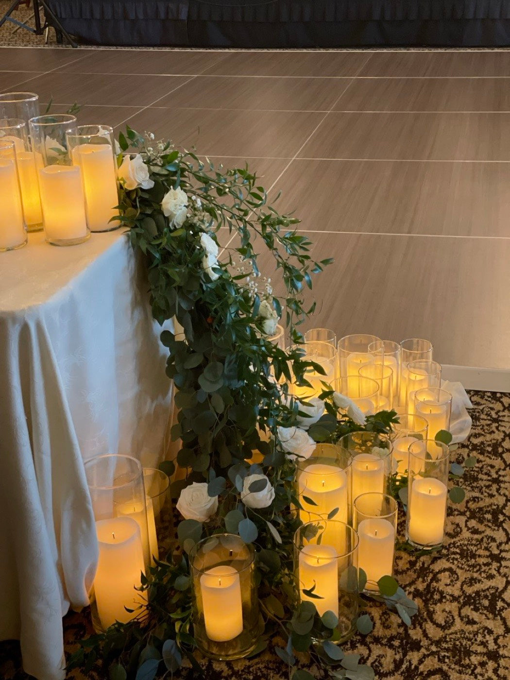 Tall white arrangement by Novapetal Flower Lab in a glass vase, with garden roses, stock and trailing greenery, beside a wooden door
