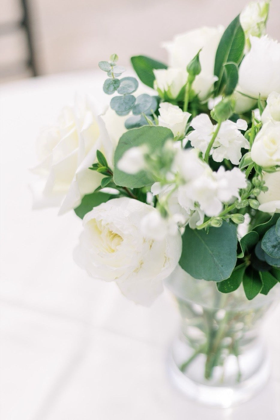 White and green bridal arrangement by Novapetal Flower Lab with peony, sweet pea and eucalyptus in a glass vase on a linen table