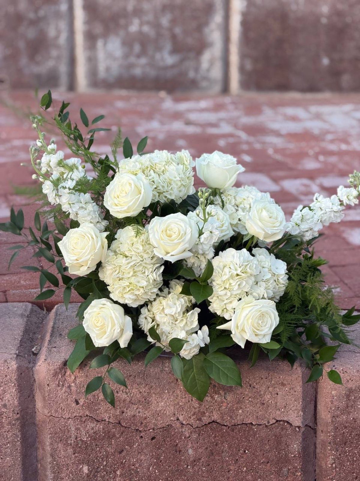 Close view of a white rose, hydrangea and stock arrangement by Novapetal on the brick ceremony steps